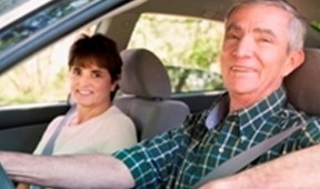 a senior couple sitting in their car with their seat belts on smiling for a photo