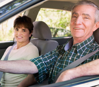 A senior couple sitting in their car with their seat belts on smiling for a photo